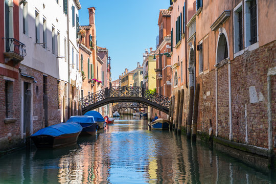 Venice canal with bridge and old brick buildings. Anchored boats in Venice canals with bridge clear sky and colorful buildings.