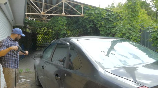 Man washing his black car near the house.