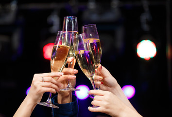 Clinking glasses of champagne in hands on bright lights backgrou
