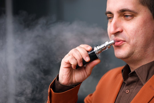 Young man smoking electronic cigarette on background of building