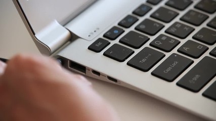 Woman's hands connecting battery charger and usb cable to laptop computer