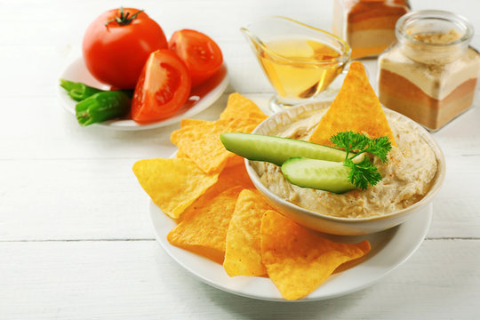 Ceramic bowl of tasty hummus with chips, oil and vegetables on table