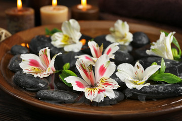 Fototapeta na wymiar Spa wooden bowl with water, flowers and stones closeup