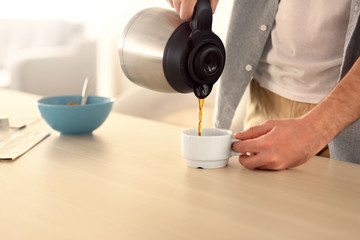 Young man pouring coffee into cup in kitchen