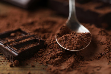 Spoon with cocoa powder and dark chocolate on table