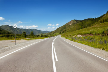 Straight road goes to horizon on background of sky and mountains. Altay mountains, Siberia, Russia.