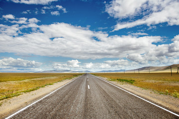 Straight road goes to horizon on background of sky and mountains. Altay mountains, Siberia, Russia.