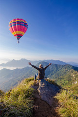 Obraz premium man on top of mountain. Phu cheefa park Chiangrai Thailand. Colorful hot-air balloon flying over the mountain.
