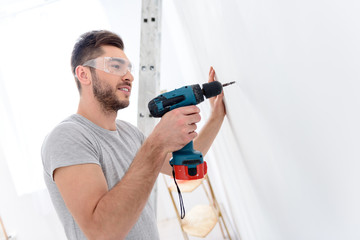 Young guy drilling white wall