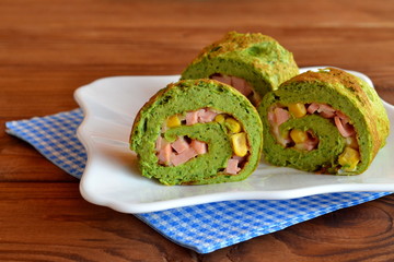 Delicious sliced omelet on a plate. Omelet made with eggs, milk, spinach, flour and salt. Omelette rolls with sausage, cheese, corn. Creative egg appetizer recipe. Unusual breakfast idea. Wooden table