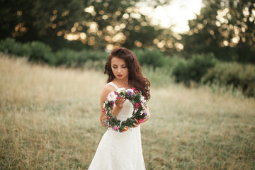 Bride. Beautiful young blond woman in the park with flower wreath and bouquet on a warm summer day