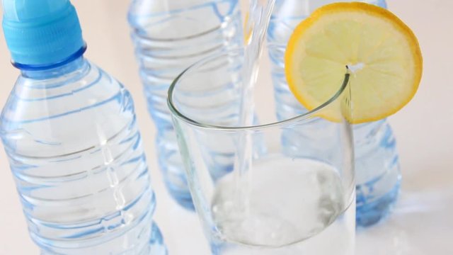 Glas wird gef&uuml;llt mit Mineralwasser, Eis und Zitrone