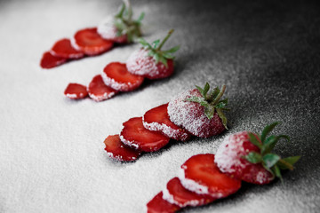 Beautiful sliced strawberries powdered sugar on black backfround. Closeup. Copy space