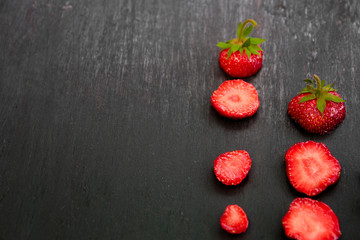 Sliced strawberries with leaves on black backfround. Top view, frame. Copy space. Summer fruit food frame.