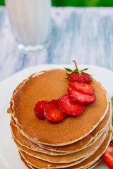 Closeup of pancakes with fresh strawberry and mint near glass with milk on white plate on pink wooden background. Stack of pancakes on the table.