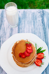 Pancakes with fresh strawberry and mint near glass with milk on white plate on pink wooden background  in garden or on nature background.  Stack of pancakes on the table.