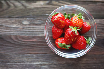 Fresh juicy strawberries in glass bowl. Rustic wooden background. Top view, place for text.