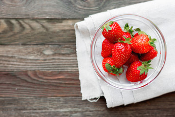 Fresh juicy strawberries in glass bowl. Rustic background with homespun napkin. Top view. Place for text.