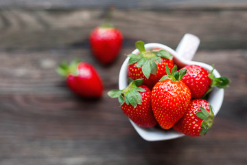 Fresh juicy strawberries in cup shaped as a heart, symbol of love. Rustic wooden background. Top view, place for text.