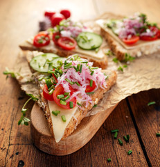 Vegetarian sandwich with cheese, cherry tomatoes, cucumber, radish and fresh chives on wooden board