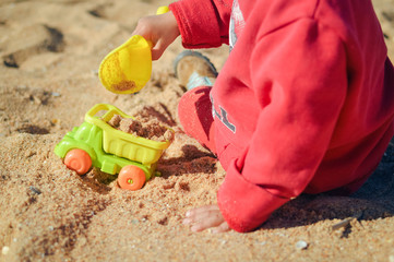 Kid having fun outdoors happy playing with his truck toys on a sunny summer day background sandy