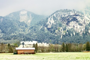 Barn of farmhouse. Spring snow in meadows bellow mountains.