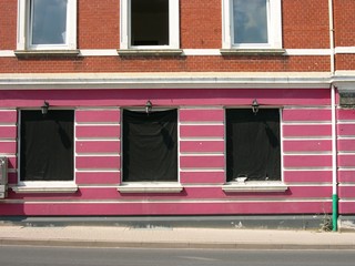 Schwarz verhangene Fenster einer ehemaligen Sexbar mit lila Fassade im Sommer bei Sonnenschein in...