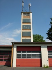 Die Feuerwehrstation mit roten Industrietoren, Segmenttoren und Schlauchturm für den Mobilfunk vor...