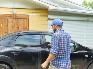 Man washing his black car near house.