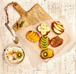 Various fruit sandwiches with banana, kiwi, apple, apricot. Healthy organic and vegan breakfast, on white wooden background. Rustic style