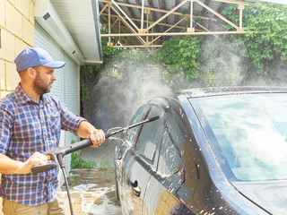 Man washing his black car near house.