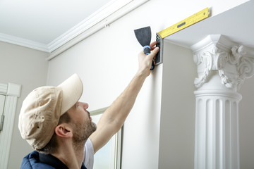 Worker holds putty knife and measures the wall corner using metal angle.  Finishing work.