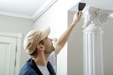 Male holds putty knife on the wall near the wall corner. Finishing work.