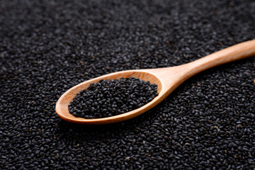 Black sesame  in wooden spoon on sesame background.