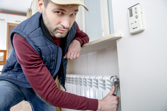 Male plumber repairing radiator with wrench. Man looking at the camera. Close-up.