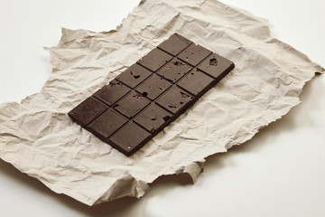 Artisan homemade organic healthy chocolate bar on craft paper, isolated on white table, side view