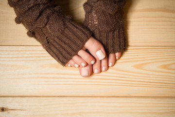 Beautiful beige pedicure. Legs in brown knitted socks on a wooden floor