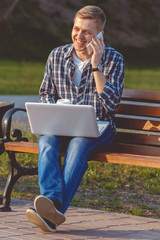 Fototapeta premium A young male businessman with a laptop and telephone. Remote work outdoors