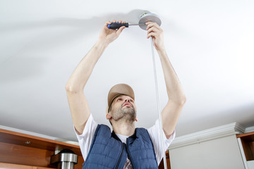 A male electrician fixing light on the ceiling with screwdriver. Close-up.