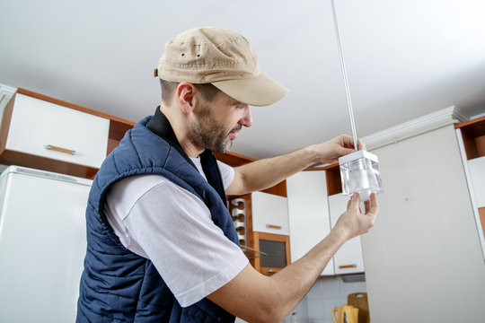 A male electrician fixing light on the ceiling. Worker changing a light bulb in the kitchen. Close-up.
