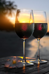 Romantic beach scene: two glasses of red wine at sunset near water