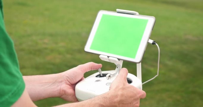 A man uses a RC controller for a drone or UAV outside in an open field. Green screen generic tablet with optional corner markers for advanced screen tracking.  	