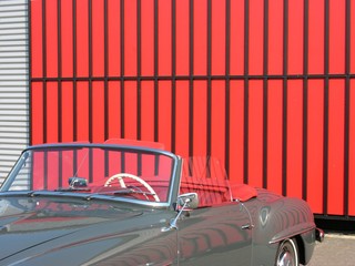 Dunkelgraues deutsches Cabriolet der Fünfziger Jahre mit rotem Interieur vor rotem Industrietor im...