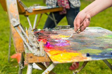 Male hand mixing oil paint on an old multiclored palette