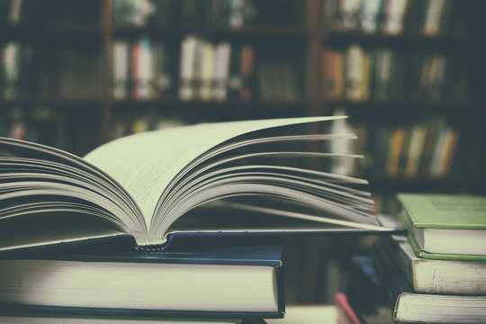Close up of open book and Stack of books on desk with vintage filter blur background