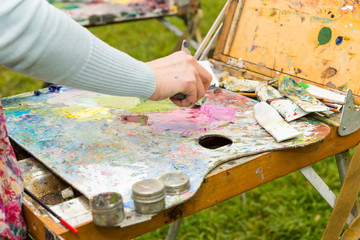 Female artist's hand mixing colors with a paletteknife in a park