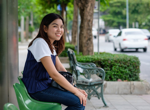 Young Woman Standing At Bus Stop On Street City. Asian Woman Waiting For Bus. Woman Student In Private Dress Standing At Bus Stop. Public Transport Stop In Thailand. Bus Stop On Street In Asian.