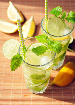 Refreshing summer drink with lemon, lime, mint and ice in glasses, selective focus, outdoor, healthy concept