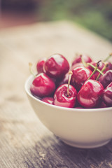 Reife Kirschen in weißer Porzellanschale, auf rustikalem Holz