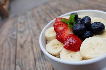 Very delicious acai bowls with fresh fruit strawberry, blueberry, banana and peppermint leaves on top in cute white cup on the wooden table. this smoothie dessert is good for summer in Hawaii.